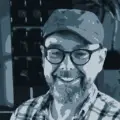 Illustration of Bjarne at his desk at Codeally. Bjarne wears a cap, glasses, a beard and a big smile.